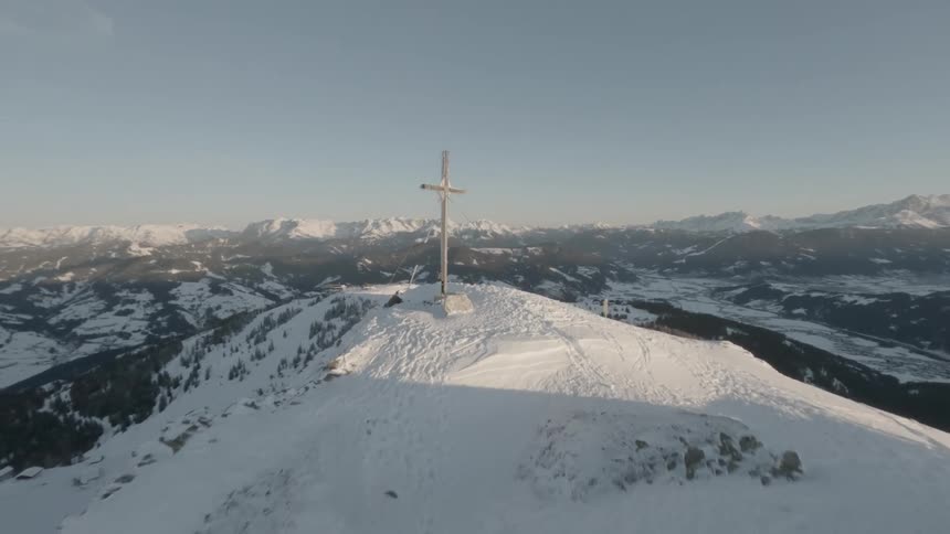 A large cross stands atop a snowcovered mountain peak