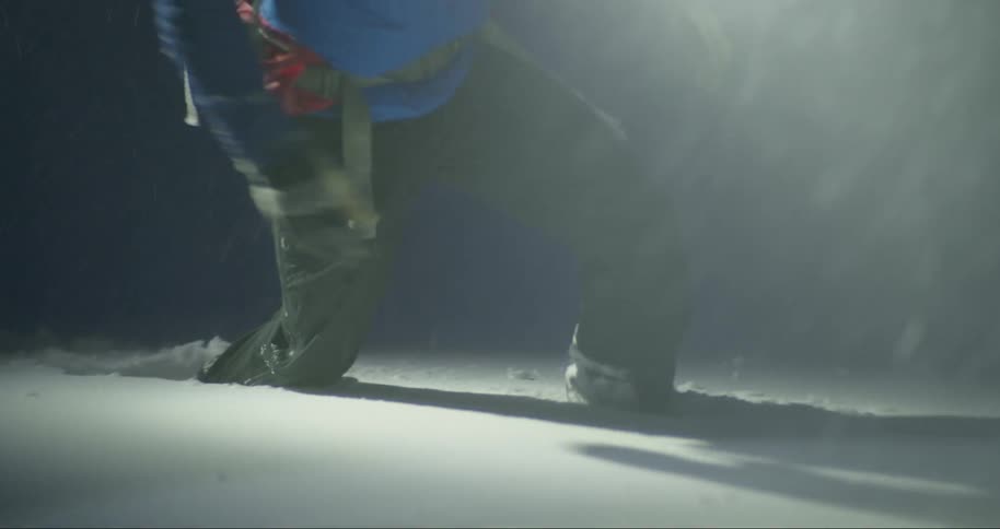 A person in dark pants and boots walking through snowy ground at night