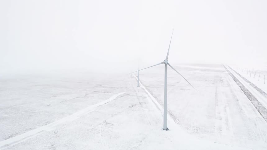 Wind turbines stand on snow covered ground on a winter day
