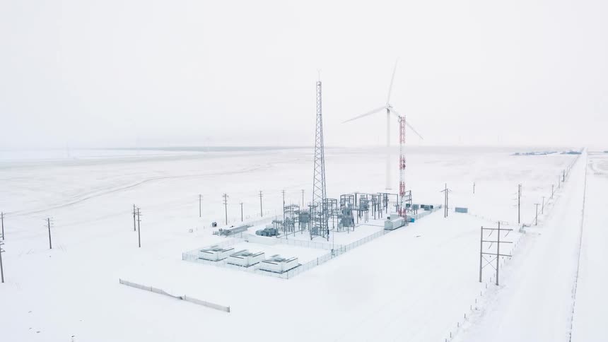 A battery grid energy storage station and wind turbine on snowy landscape