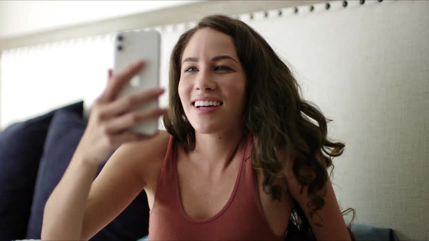 Woman lying in bed gets up taking her cell phone and smiling while talking