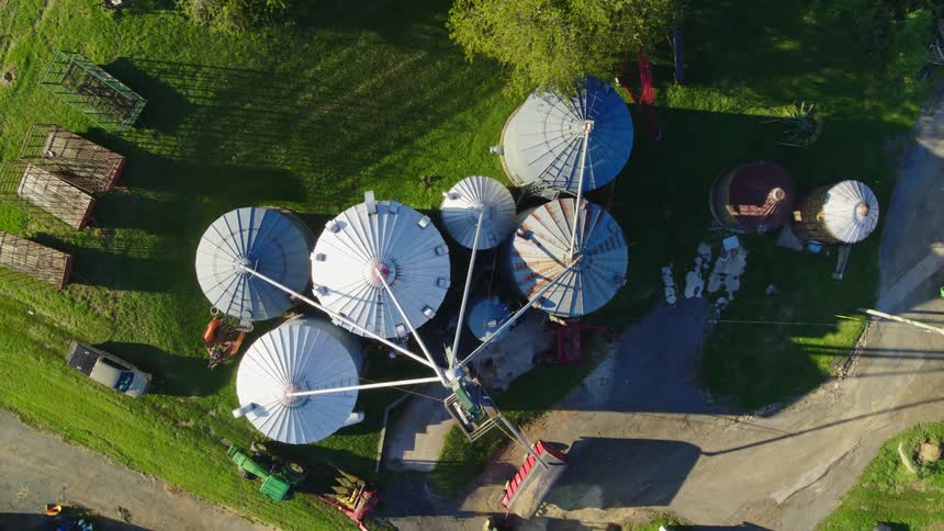 Six large silos next to each other are with tubes connected to a vehicle in a rural region
