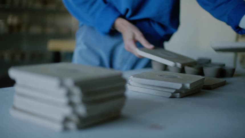 A woman stacks pieces of flat pottery