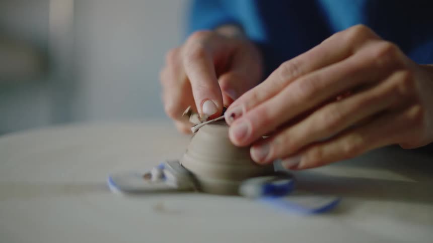 A persons hands that are forming a clay object that is rotating
