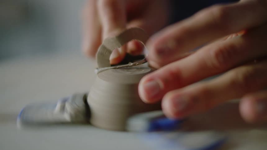 A womans hands making and modeling a small clay vase in a rotating machine