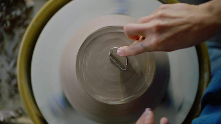 Hands of a woman holding a clay pot on a rotating apparatus