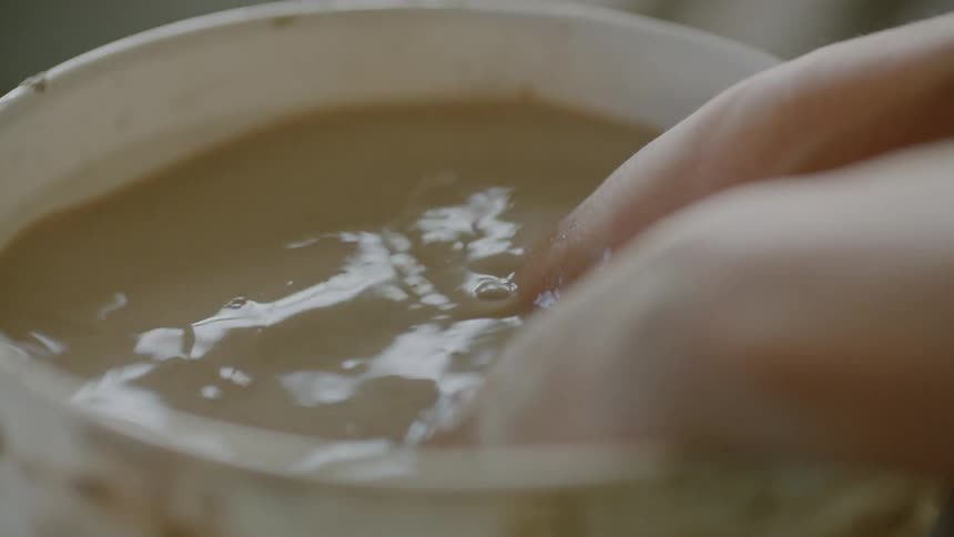 A woman dips her hands into water while working with clay pottery