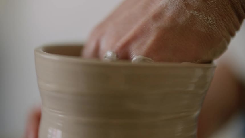 A womans hand shaping clay on a wheel