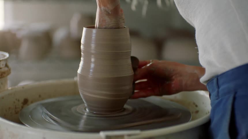 A woman shapes clay on a spinning pottery wheel into a vase