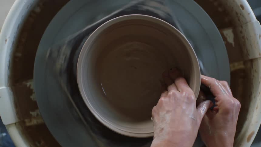A persons hand discussing a clay vase