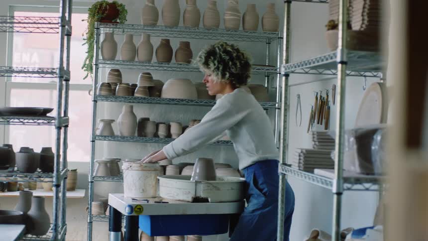 A woman with short hair and is modeling clay that is spinning over a container