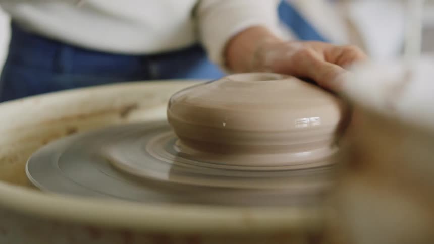 Woman with a lump of clay and sculpting a vase on a machine