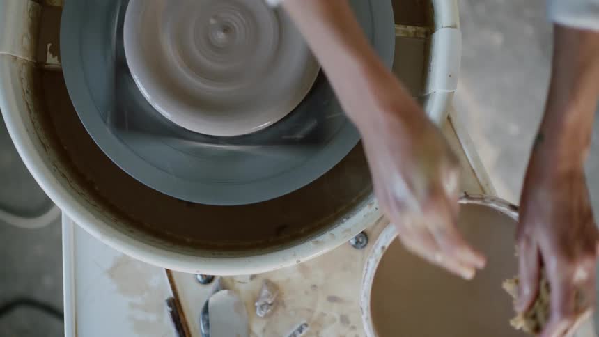 Female potter shaping clay on pottery wheel pauses briefly to wet her hands