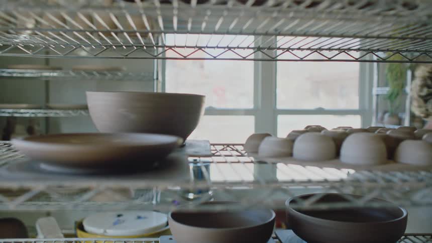 A white woman puts a pottery bowl on metal shelving