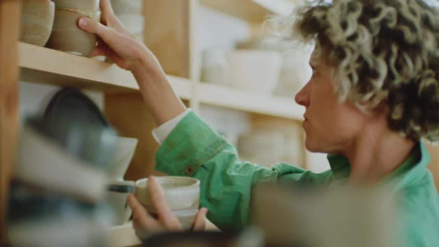 A female arranges sculpted mugs on the shelve at midday