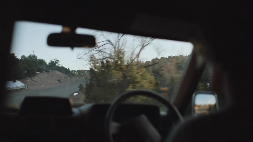 A person in a car is driving on a street in a rural area