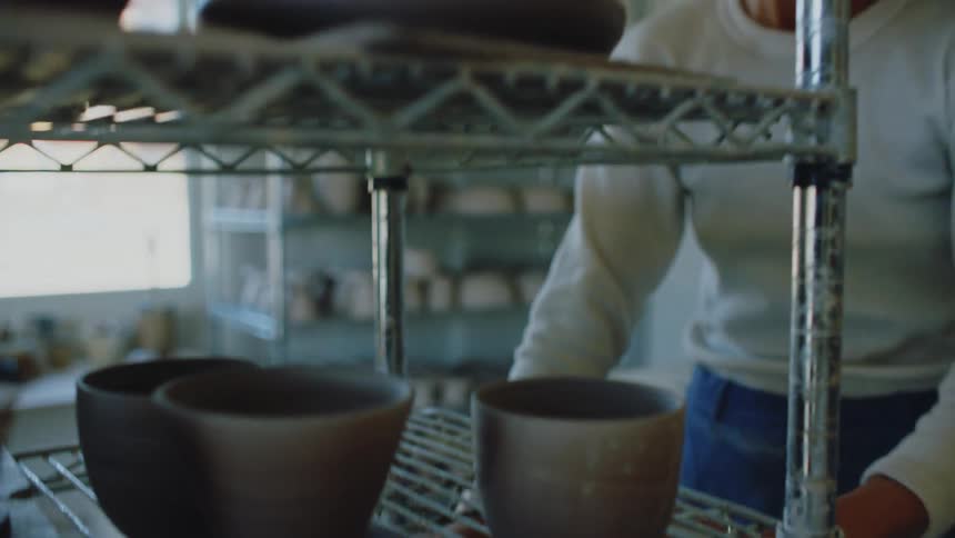 Lady smiling while arranging ceramics on the shelve