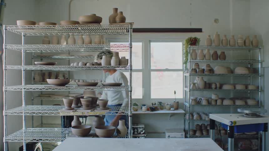A white woman places pottery pieces on shelves