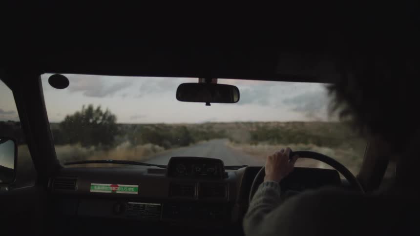 Inside a car with a view of the dashboard and the woman driving on a simple road