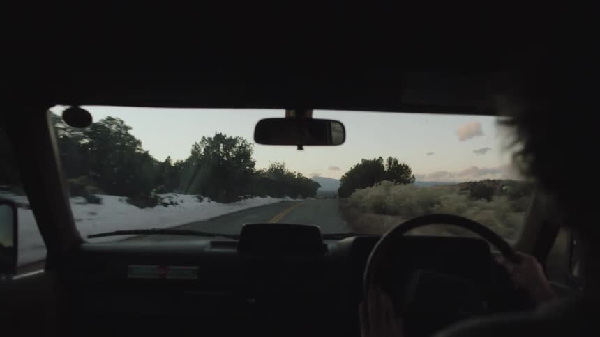 A woman driving down a road with snow on either side of it