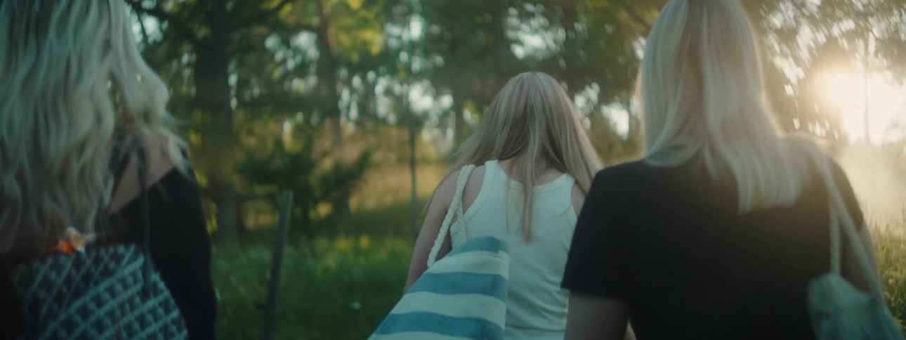 View of women from the back walking on a lawn with trees during the day