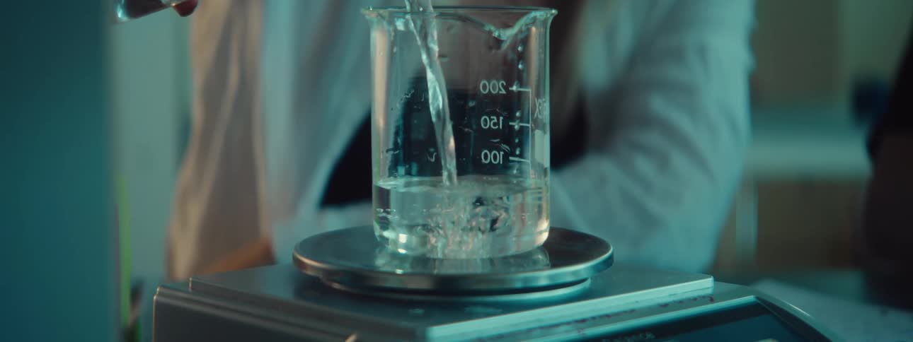 A person is using a digital scale to weigh a beaker containing a liquid