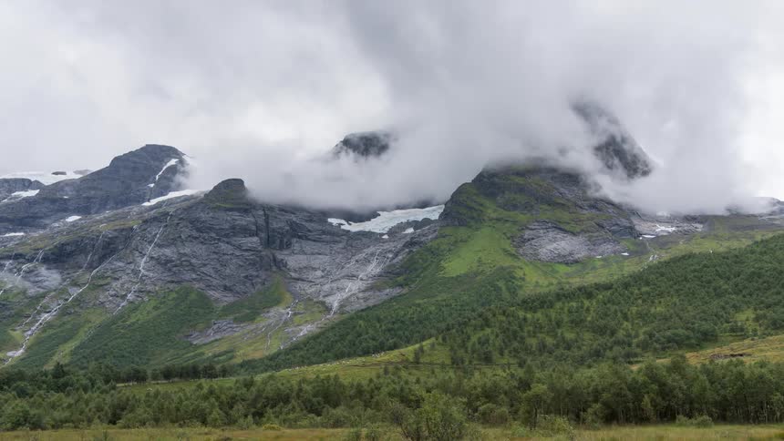 A time lapse reveals clouds lingering over a snow covered mountain