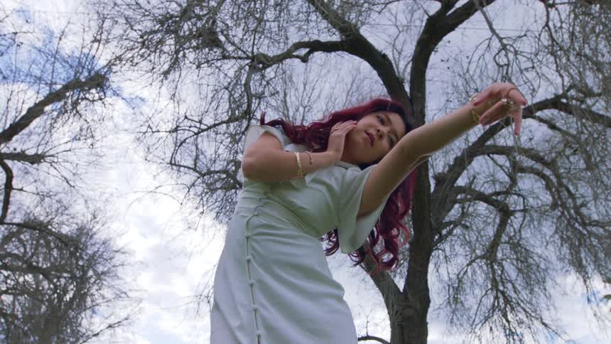 Lady in white gown and red hair dancing under a withered tree at midday