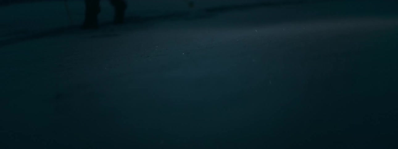 A person with a flashlight walks through snow at night