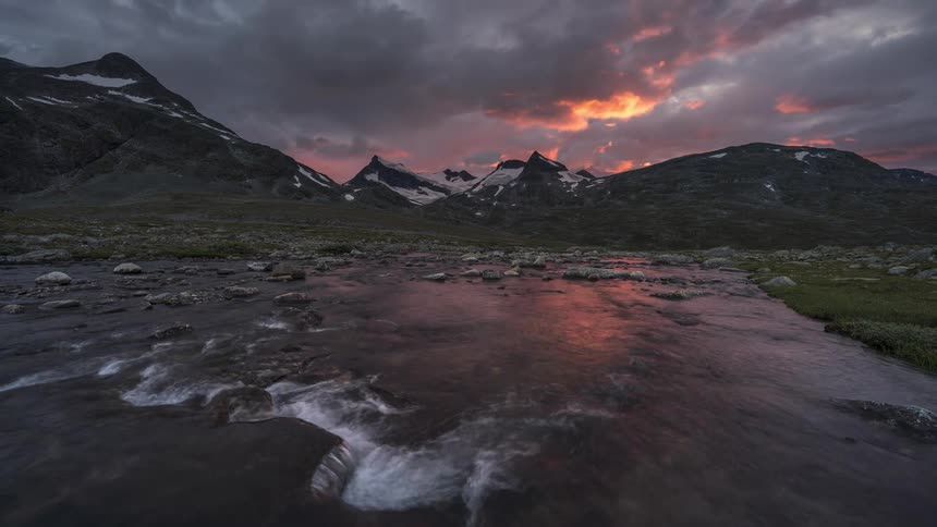A flowing river with rocky shores next to the mountains at sunset