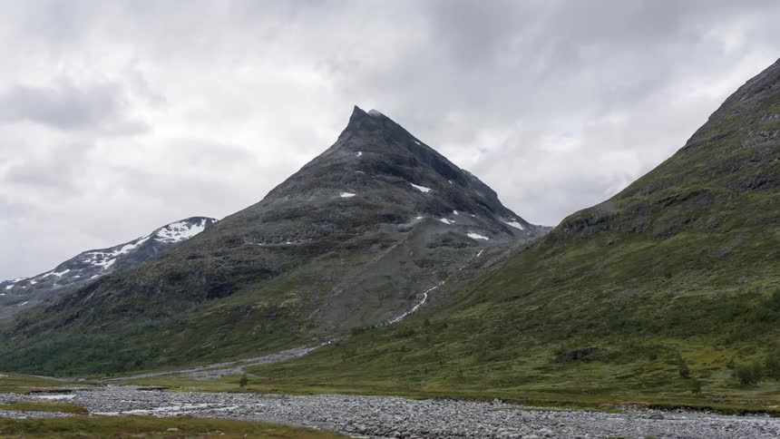 Timelapse landscape of rocky mountains with rivers and snow on a cloudy day
