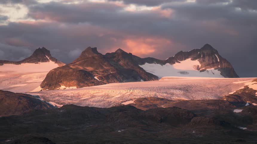A time lapse shows thick clouds passing over a snow covered mountain range
