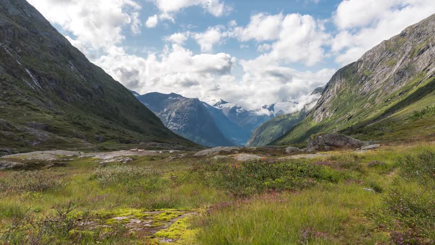 Sheep in green valley surrounded by high mountains as the clouds floating in the sky