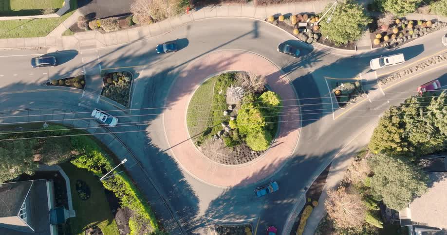 Top down twist over cars driving through a neighborhood roundabout during the morning commute
