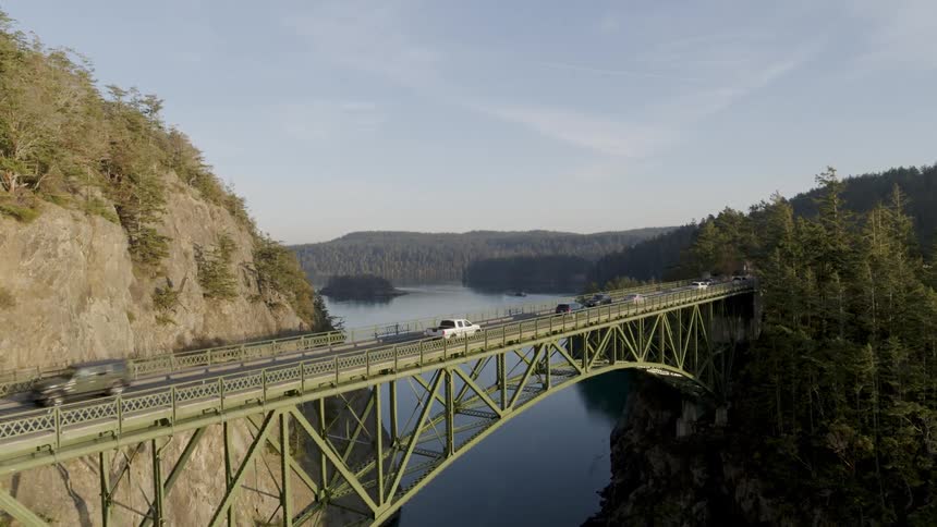 Cars and trucks cross a bridge high over water amidst beautiful scenery