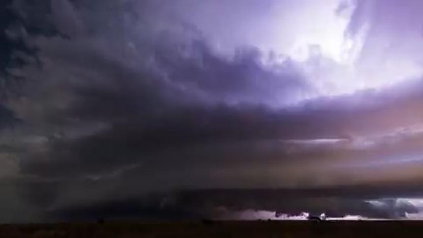 Lightning illuminates a dark stormy night sky as a supercell pours rain across the land