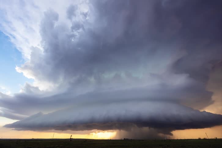 A supercell storm pours rain on the land as it moves across the sky