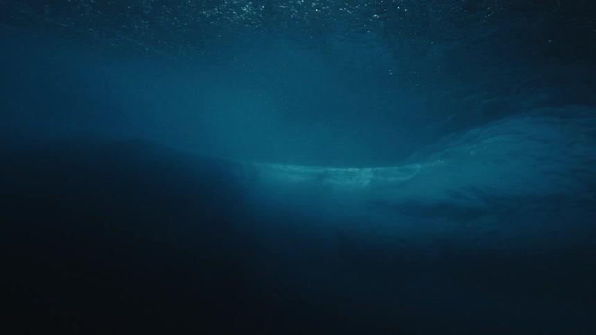From below the surface of the ocean a large wave is seen passing overhead