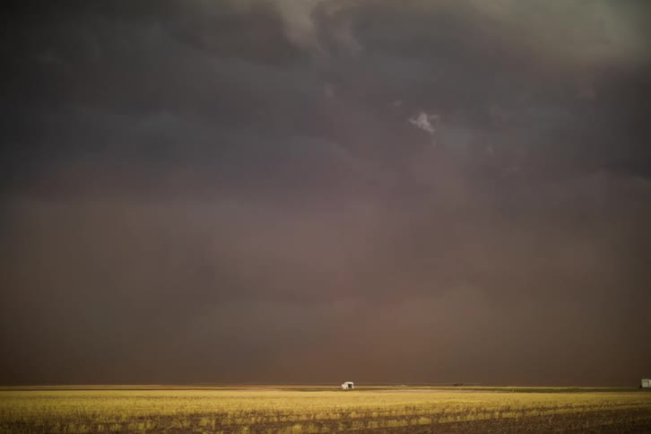Dark clouds gather in the sky above the brown field casting shadows over the lush landscape