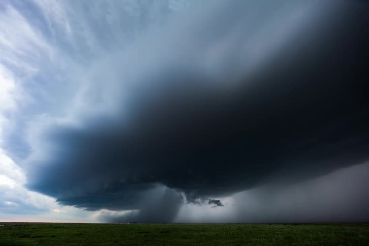 Dark storm clouds pour down rain and move across the land as lightning flashes