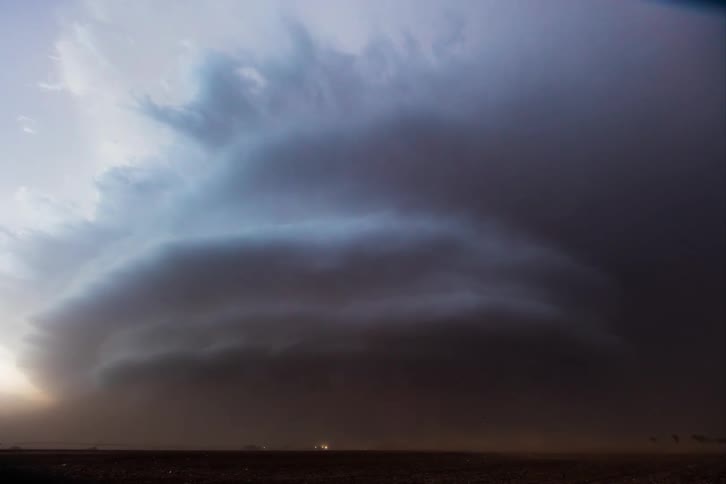Dark supercell storm moves over the land and pours down rain as lightning flashes