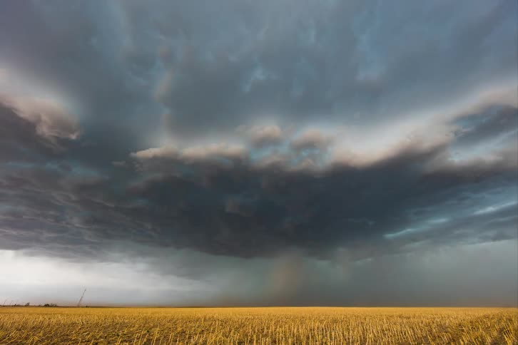 Storm clouds pour rain on rural land as lightning flashes and strikes the ground
