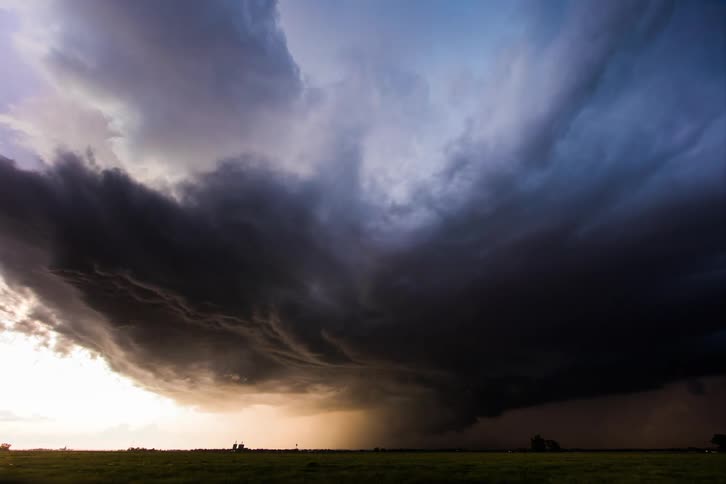 Storm clouds form and blacken the sky over grassy farmland