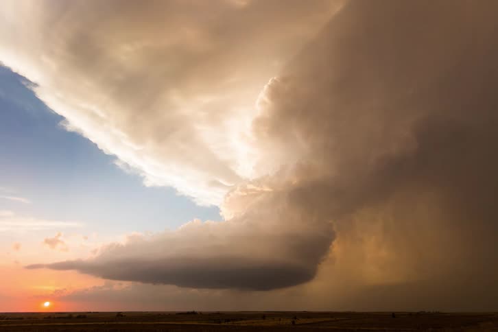A supercell storm in rotation as it moves over the land and the sun sits on the horizon