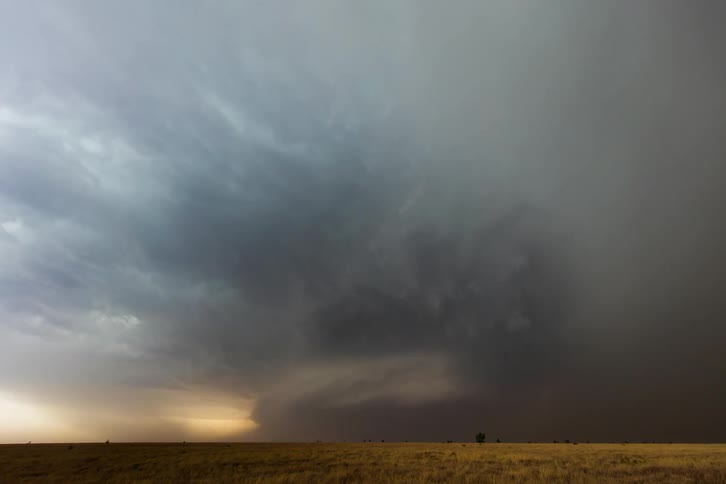 Storm clouds move across the sky as lightning flashes and a supercell is in rotation on the ground