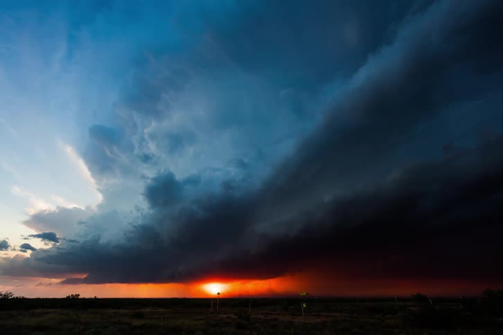 Dark storm clouds move across the sky as the sun sets on the horizon