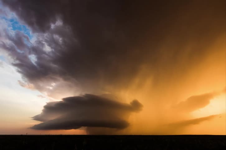 A dark cloud formation looms over a landscape during sunset