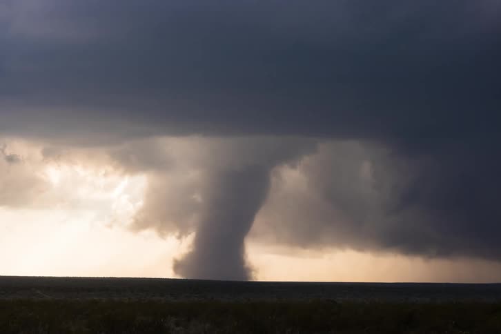 Dark storm clouds move in as a tornado funnel cloud spins across the land and lightning flashes