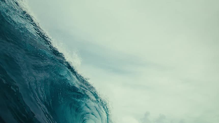A huge wave breaking on the surface of the sea and under the water there is a man swimming
