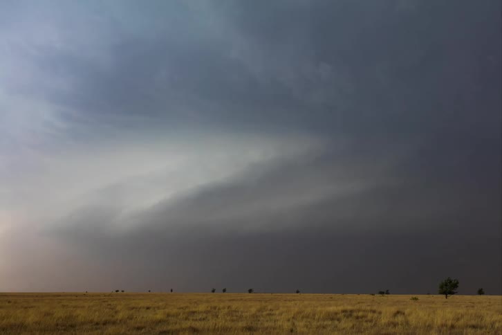 Storm clouds turn in rotation as they move over farm land and lightning flashes and strikes the ground